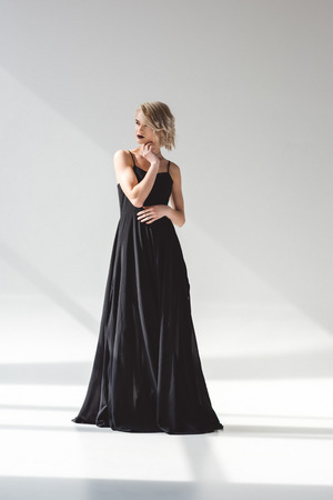 Blonde young woman posing in elegant black dress, on grey backgroundの写真素材