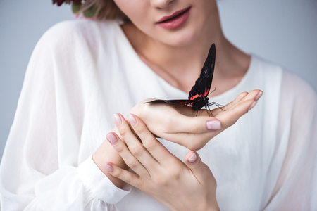 Cropped view of girl with alive butterfly on hand, isolated on grey backgroundの写真素材