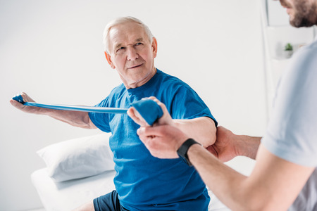 cropped shot of rehabilitation therapist assisting senior man exercising with rubber tapeの写真素材