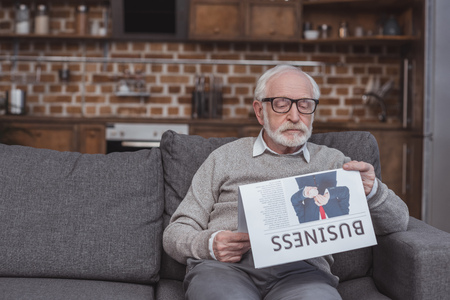 handsome grey hair man reading business newspaper on sofa at homeの写真素材