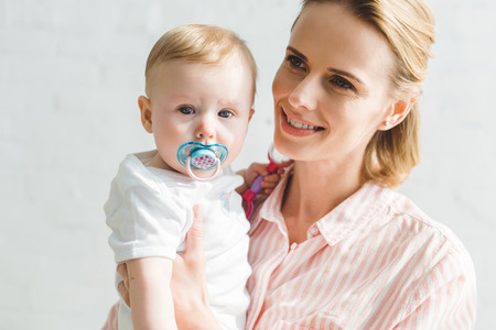 Smiling mother holding infant daughter with baby dummy