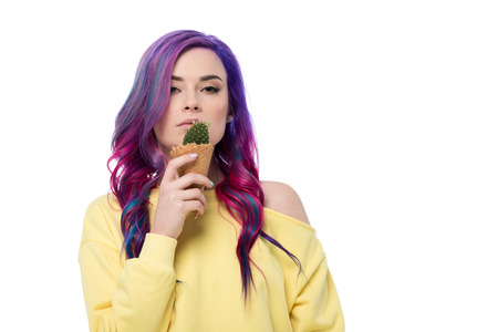 Beautiful young woman with purple hair holding cactus plant in ice cream waffle cone isolated on...
