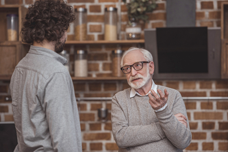 adult son and senior father talking at kitchen homeの写真素材