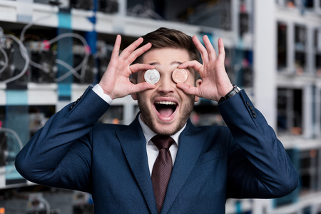 happy young businessman covering eyes with bitcoins at cryptocurrency mining farmの写真素材
