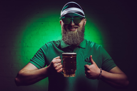smiling bearded man holding glass of beer and showing thumb up, st patricks day conceptの写真素材