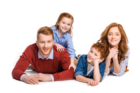 happy red haired family with two kids lying together and smiling at camera isolated on whiteの写真素材