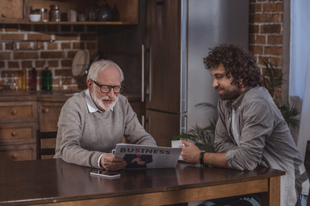 adult son and senior father reading business newspaper at homeの写真素材
