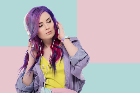 beautiful young woman with colorful hair in purple trench coat listening music with headphonesの写真素材