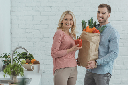 portrait of grown son and mother with paper bag full of fresh vegetables for dinner at homeの写真素材