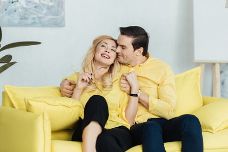 Embracing man and woman sitting on yellow sofaの写真素材