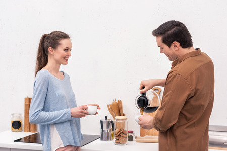 handsome man pouring coffee for wife and himself in morningの写真素材
