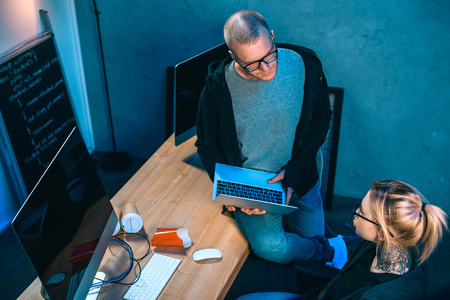high angle view of couple of hackers working on malware together in dark roomの写真素材