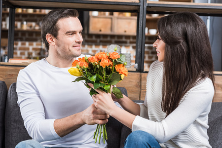 multiethnic couple looking at each other while man presenting bouquet of flowers to womanの写真素材