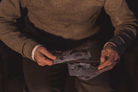 cropped image of senior man holding old photos at homeの写真素材