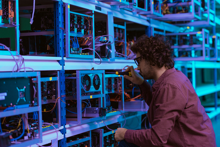 young computer engineer repairing at cryptocurrency mining farm with screwdriver