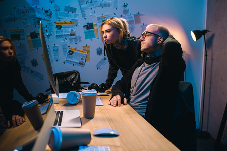 couple of hackers looking at computer screen together in dark room