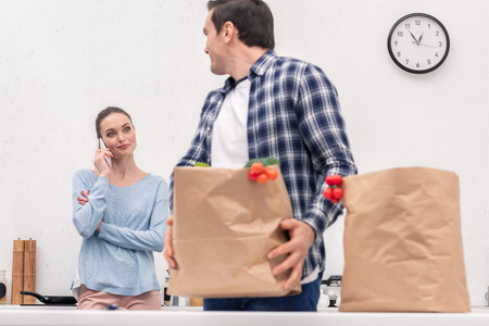 adult man carrying paper bag from grocery store while his wife talking by phoneの写真素材
