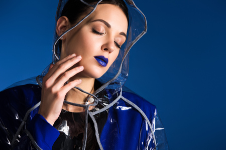 Dreamy woman with blue lipstick wearing raincoat isolated on blue backgroundの写真素材