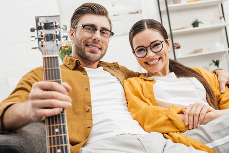 happy relaxed couple with guitar sitting on couch at homeの写真素材