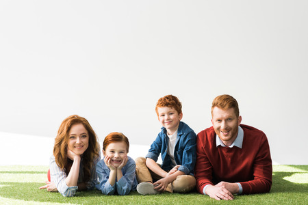 beautiful happy redhead family lying on grass and smiling at camera on greyの写真素材
