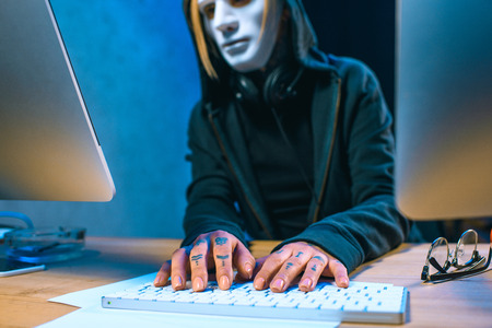 close-up shot of masked female hacker with tattoos on hands developing malware