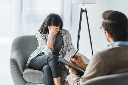 Stressed woman sitting in chair at male doctor officeの写真素材