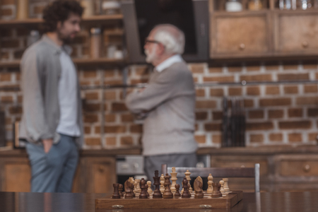 adult son and senior father talking at kitchen with chessboard on foregroundの写真素材