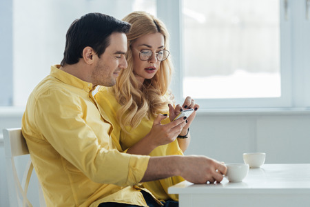 Man and woman drinking coffee and looking at smartphone screenの写真素材