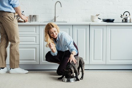Man brewing coffee and blonde woman stroking french bulldog on kitchen floorの写真素材