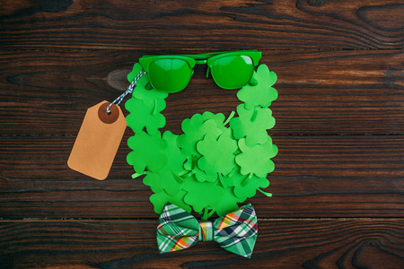 top view of bearded face symbol made of green clovers, sunglasses, blank tag and bow tie on wooden tableの写真素材