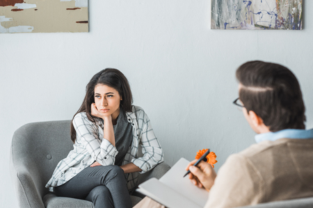 Young woman visiting psychotherapist in cozy doctor officeの写真素材