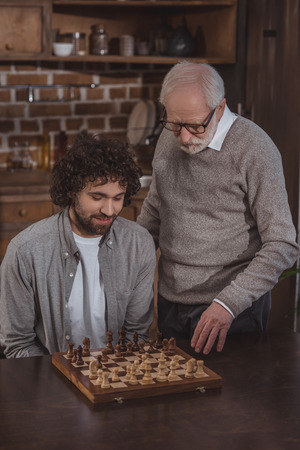 adult son and senior father playing chess together at home