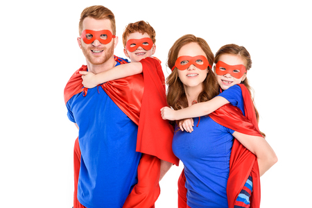 super parents piggybacking happy kids in masks and cloaks isolated on whiteの写真素材