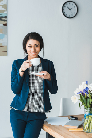 Smiling female manager enjoying coffee during break in modern officeの写真素材