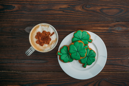 top view of tasty cappuccino and cookies in shape of clovers on wooden tableの写真素材