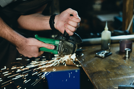 close-up partial view of man cutting metal with angle grinder in workshopの写真素材