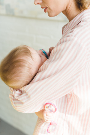 Cropped view of mother holding infant daughter with baby dummy and toyの写真素材