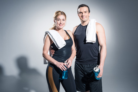 Athletic man and woman with towels holding sport bottles on grey backgroundの写真素材