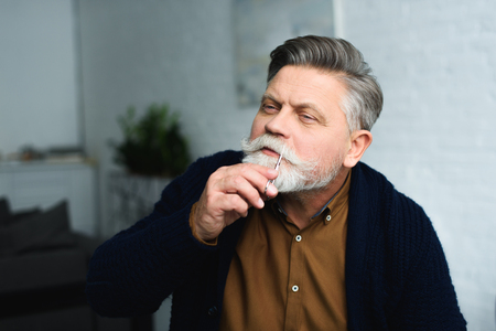 handsome senior man trimming moustache with scissors at homeの写真素材