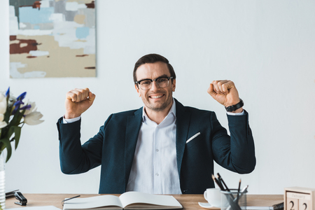 Excited businessman in glasses by working tableの写真素材
