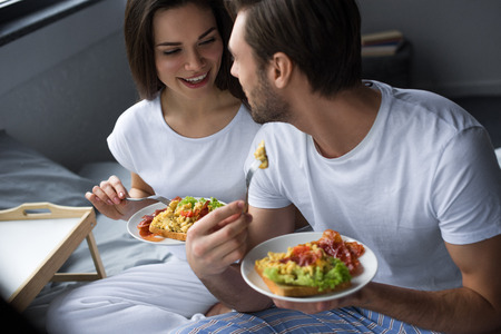 Smiling man and woman having breakfast in bedの写真素材
