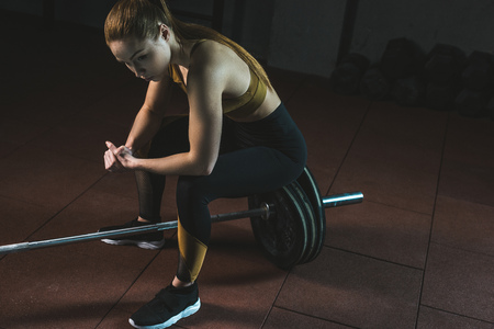 Frustrated young sportswoman sitting on barbell in gymの写真素材