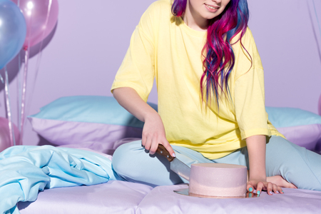 cropped shot of smiling young woman cutting birthday cake in bedの写真素材
