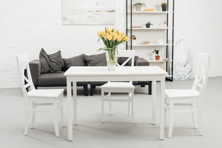interior of white living room with yellow tulips in vase on table