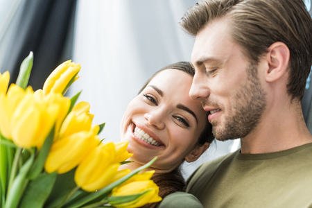 close-up shot of man presenting yellow tulips to happy girlfriendの写真素材