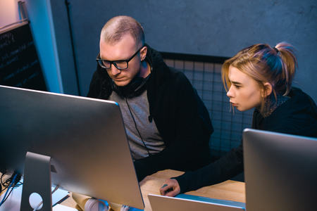 young couple of hackers looking at computer screen together at workplaceの写真素材