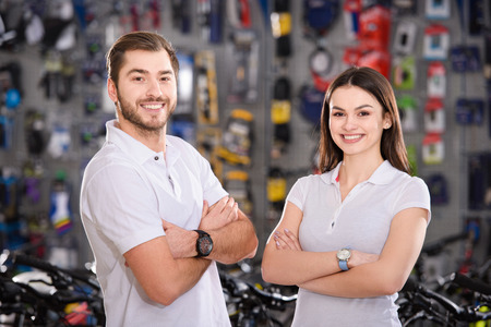 confident young workers standing with crossed arms and smiling at camera in bike shopの写真素材