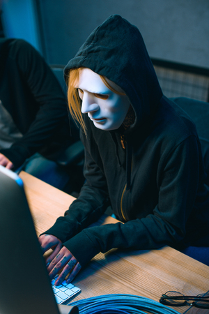 high angle view of hacker in mask working with computer to develop malwareの写真素材