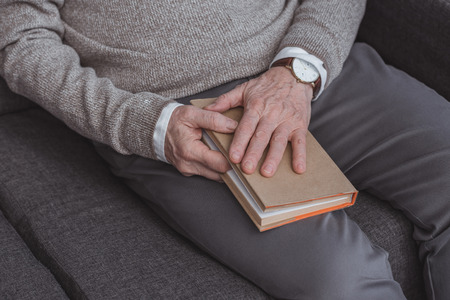 cropped image of grey hair man holding book at homeの写真素材