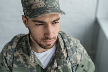 portrait of soldier in military uniform looking away against white brick wallの写真素材